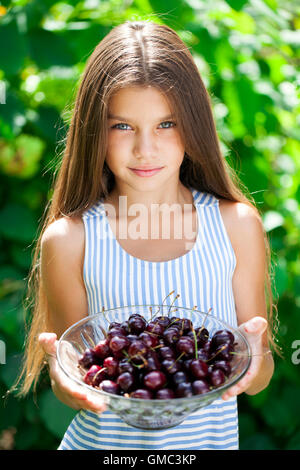 Beautiful brunette little girl holding a bowl of cherries in the garden Stock Photo