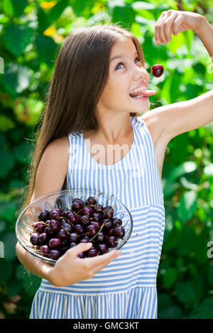 Beautiful brunette little girl holding a bowl of cherries in the garden Stock Photo