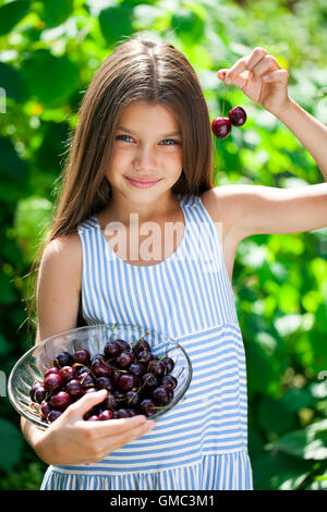 Beautiful brunette little girl holding a bowl of cherries in the garden Stock Photo