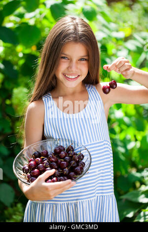 Beautiful brunette little girl holding a bowl of cherries in the garden Stock Photo