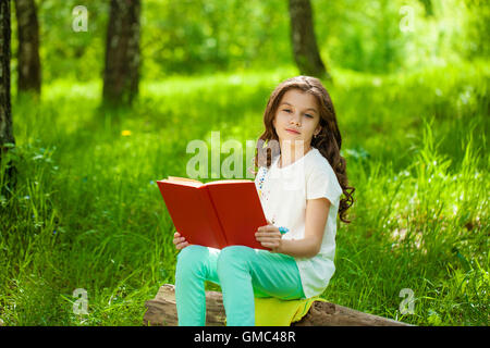 Charming little girl in forest with book on the background of summer park Stock Photo
