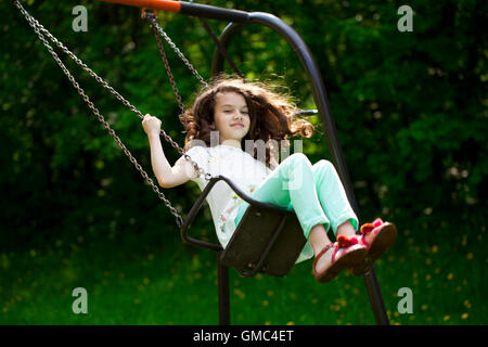 Happy Little girl on a swing in the summer park Stock Photo