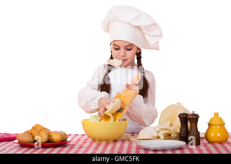Portrait of a little girl in a white apron and chefs hat shred cabbage in the kitchen, isolated on white background Stock Photo