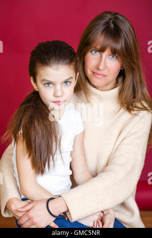 Portrait of seven year old daughter and young mother on red isolated Stock Photo