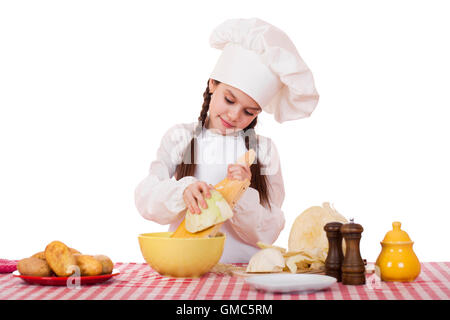 Portrait of a little girl in a white apron and chefs hat shred cabbage in the kitchen, isolated on white background Stock Photo