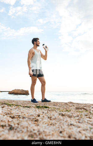 Young sporty man athlete resting after jogging at the beach and drinking water Stock Photo