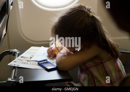 Girl child kid aged / age 4 years go on holiday / vacation & draws / draw / drawing; flying on air plane / airplane / aeroplane flight Stock Photo