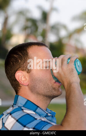 Young man drinking from a cup outside at a park wearing a plaid shirt. Stock Photo