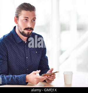 long haired handsome man looking up while holding phone Stock Photo