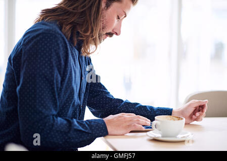 Trendy male hipster busy using his tablet on the table Stock Photo
