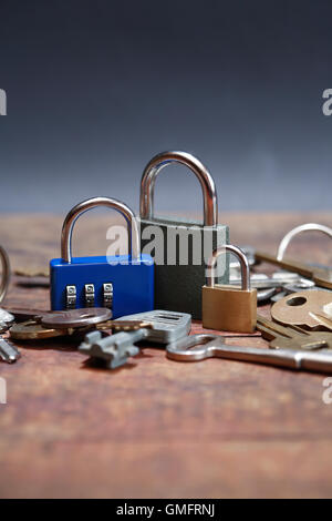 Three padlocks near keys on wooden board against dark background Stock Photo