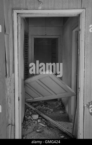 Abandoned house hallway with unhinged door and rubble on dirty floor. Black and white. Stock Photo