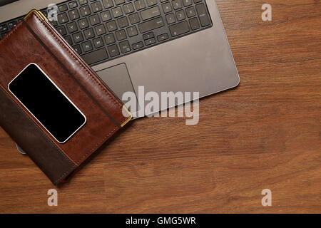 Top view of daily planner / diary, mobile phone and laptop computer, on a wooden desk. Home office concept. Stock Photo
