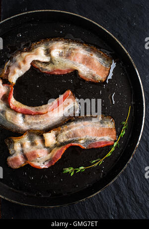 Pan of fried bacon on black slate background Stock Photo