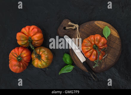 Fresh ripe hairloom tomatoes and basil leaves on rustic wooden board Stock Photo