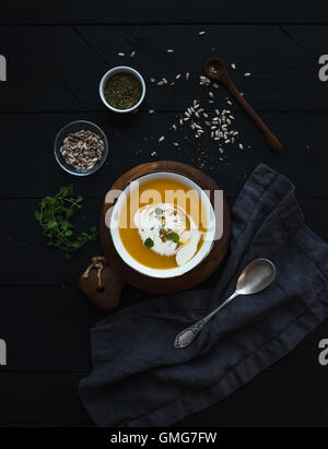 Pumpkin soup with cream, seeds and spices in rustic metal bowl over black background. Top view. Stock Photo