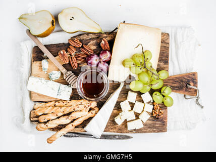 Cheese appetizer set. Various types of cheese, honey, grapes, pear, nuts and bread grissini sticks on rustic wooden board over white background Stock Photo