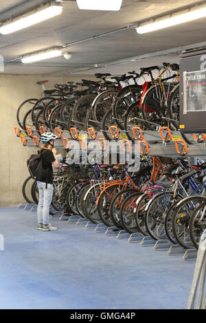 A cyclist adjusts her hat before removing her bike from the rack in a new multi-storey bike storage park in Cambridge, UK. Stock Photo