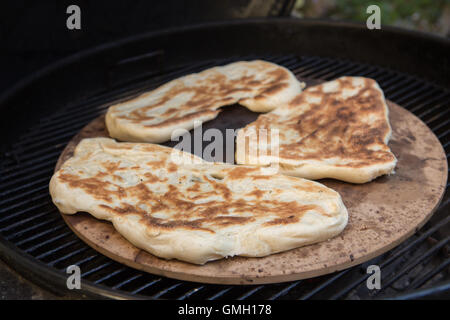 Fresh Homemade naan bread cooked outdoors on a pizza stone over a charcoal barbecue Stock Photo
