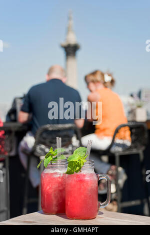 Vertical portrait of cocktails on a table of a rooftop bar overlooking Trafalgar Square in London.