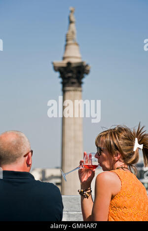 Vertical portrait of a couple enjoying a drink whilst overlooking Nelson's Column in Trafalgar Square, London, in the sunshine. Stock Photo