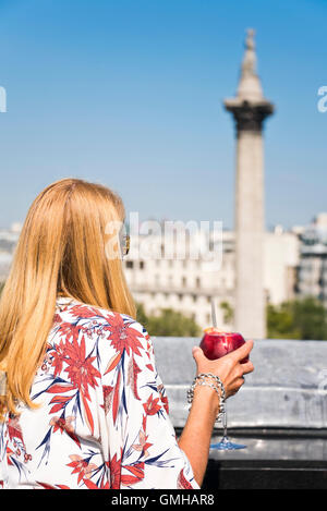 Vertical portrait of a woman enjoying a cocktail overlooking Nelson's Column in Trafalgar Square, London, in the sunshine. Stock Photo