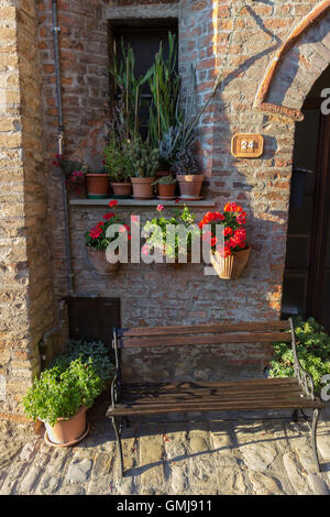 Typical old brick wall decorated with pots of flowers, plants and a small bench Stock Photo