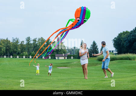 Happy family flying kite together on a green field Stock Photo