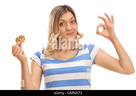 Cheerful woman eating a cookie and making an ok sign isolated on white background Stock Photo