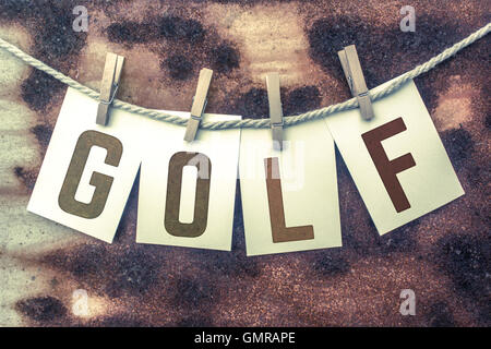 The word 'GOLF' stamped on cards and pinned to an old piece of twine over a rusted metal background. Stock Photo