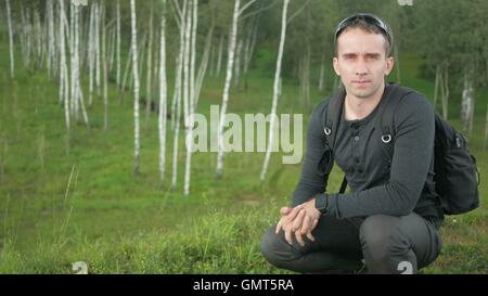 Young handsome man in a nice fitting clothes removes and wears sunglasses. Smile in camera, natural scenery Stock Photo