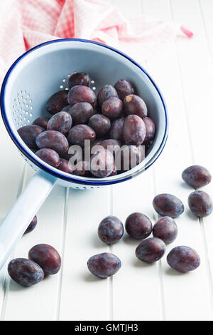 Fresh plums from garden in colander on kitchen table. Stock Photo