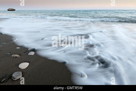 Pebbles on the beach on black sand and flowing sea water creating nice textures. Long exposure image. Stock Photo