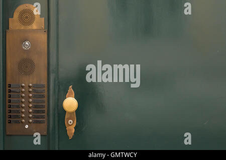 A dark green painted door with bronze door bells and a golden round door knob. Free space on the right side of the image. Stock Photo