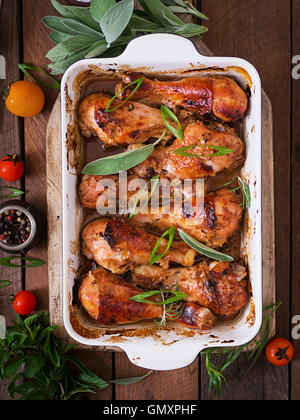 Appetizing oven baked golden chicken drumsticks in a baking dish on a wooden table. Top view Stock Photo