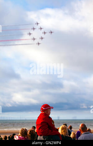 Rhyl, Denbighshire, Wales, UK. 28th August 2016. Rhyl Air Show – The annual air show at Rhyl seafront with the RAF Red Arrows. A young boy in his RAF Red Arrows jumpsuit with the Red Arrows flying by Stock Photo