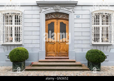 Front view of an elegantly carved light brown wooden door with ornamented gray frame and wall. Stock Photo