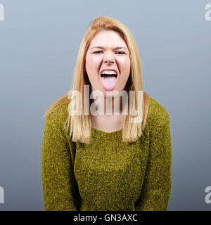 Portrait of woman sticking out her tongue against gray background Stock Photo