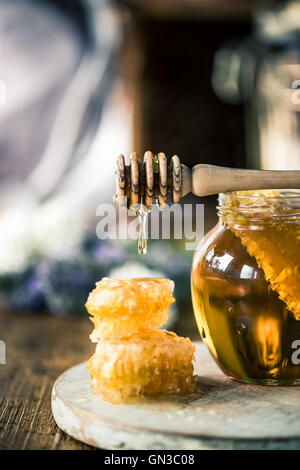 Honey dripping over vax comb on wooden table Stock Photo