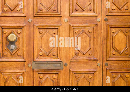 Close view of an elegantly carved light brown wooden door with square pattern and an octagonal door knob on the left side. Stock Photo