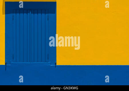 A blue wooden window closed on a yellow and blue wall in a european street. Stock Photo