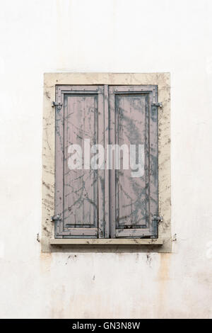 A window with closed, old, withered shutters. Traces of former vine branches still visible on the worn wood. Stock Photo