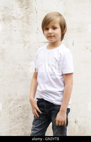 cute blond boy in jeans and a white shirt posing on wall background Stock Photo