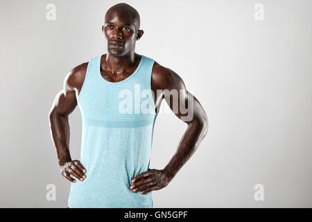 Portrait of handsome young black man with shaved head and hands on hips over grey background. Muscular african male model lookin Stock Photo