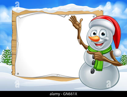 A happy Christmas snowman cartoon character in a winter scene pointing at a sign Stock Photo