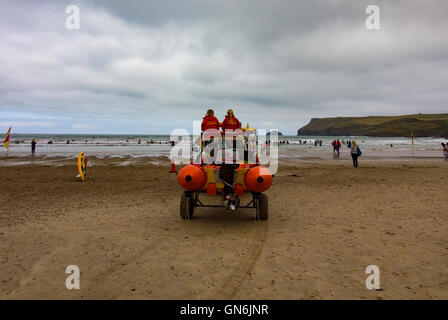 Two Female RNLI lifeguards keep watch as people learn to surf on a chilly summer morning at Polzeath Beach, North Cornwall, UK Stock Photo