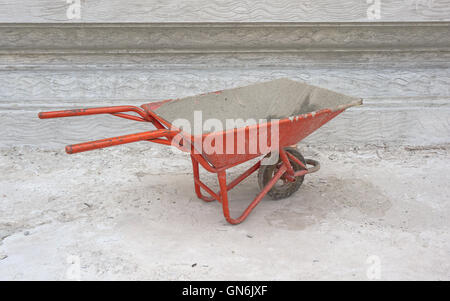 Dirty cement wheelbarrow cart at construction site with unfinished cement wall background Stock Photo