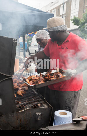 Two men preparing a chicken barbecue on an old oil drum grill at Notting Hill Carnival Stock Photo
