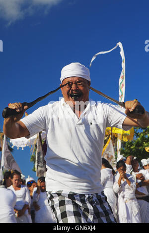 Balinese man in trance pricking himself by Kris dagger during ritual fighting dance on Melasti hindu religious ceremony Stock Photo