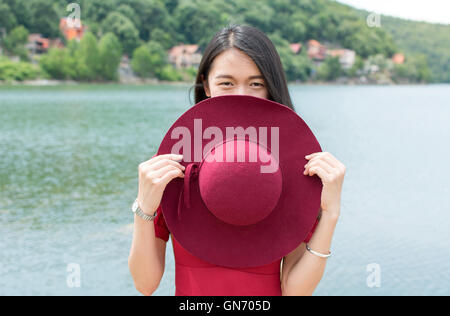 Fashionable woman holding hat standing in front of a lake Stock Photo